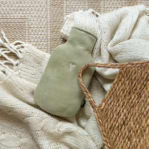 Grüne Wärmflasche aus Fleece Baumwolle mit weißem Herzstick auf einer weißen Decke.