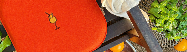 Sitzkissen aus nachhaltigem Upcycling Filz in Orange auf einem Holzstuhl mit Motiv Aperol Sprizz