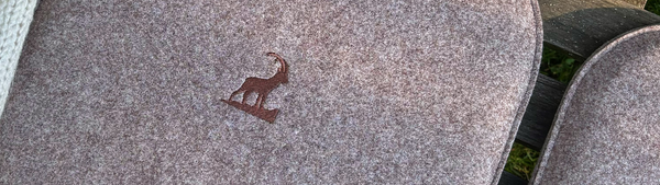 Sitzkissen aus nachhaltigem Upcycling Filz in braun auf einer Holzbank mit dem Motiv Steinbock